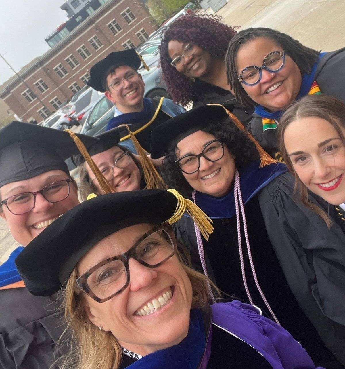 A group of professors smiling for a photo outside before graduation, wearing their commencement robes